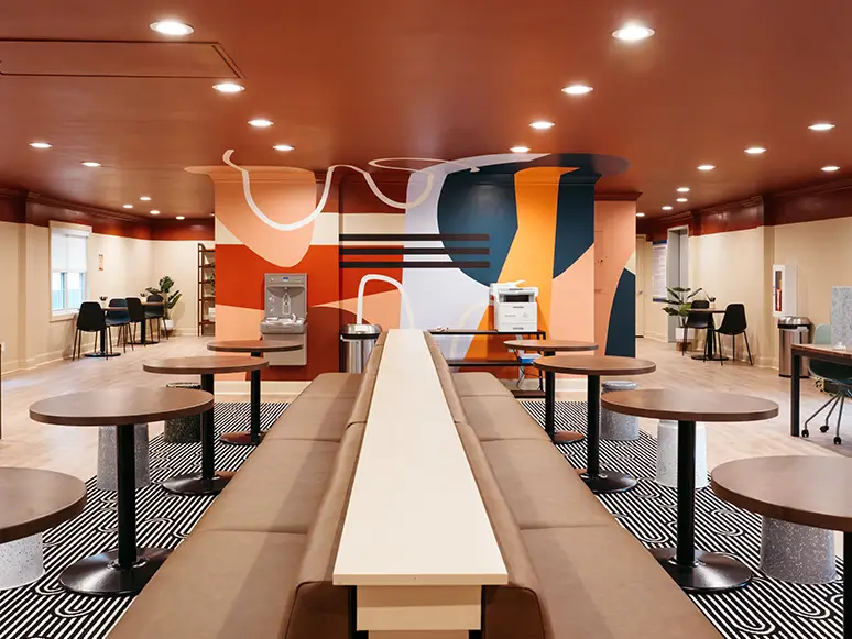 Lounge with a long bench, café tables, and a colorful mural