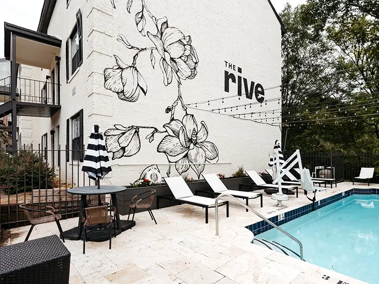 Pool with lounge chairs and umbrellas in front of a white brick mural wall