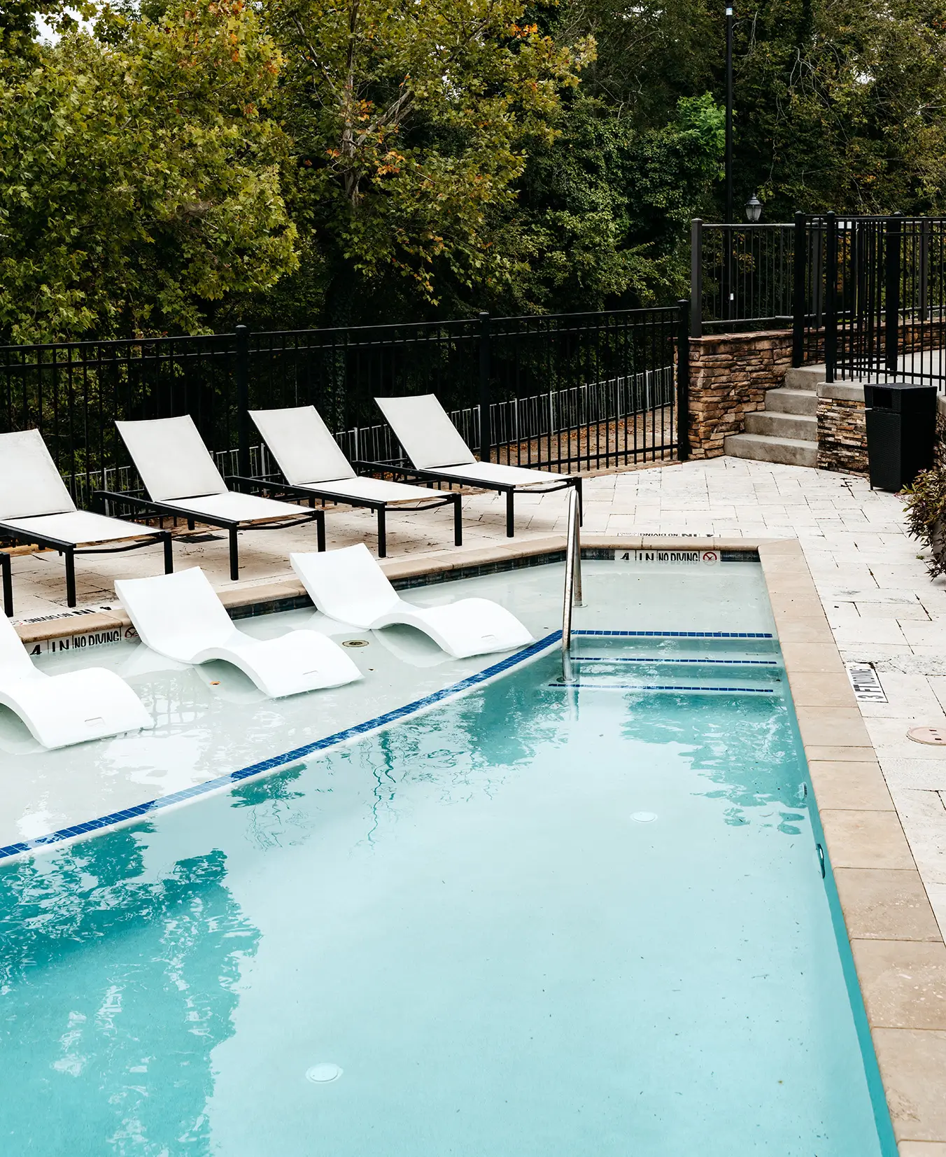 Pool with lounge chairs beside a wooded hillside