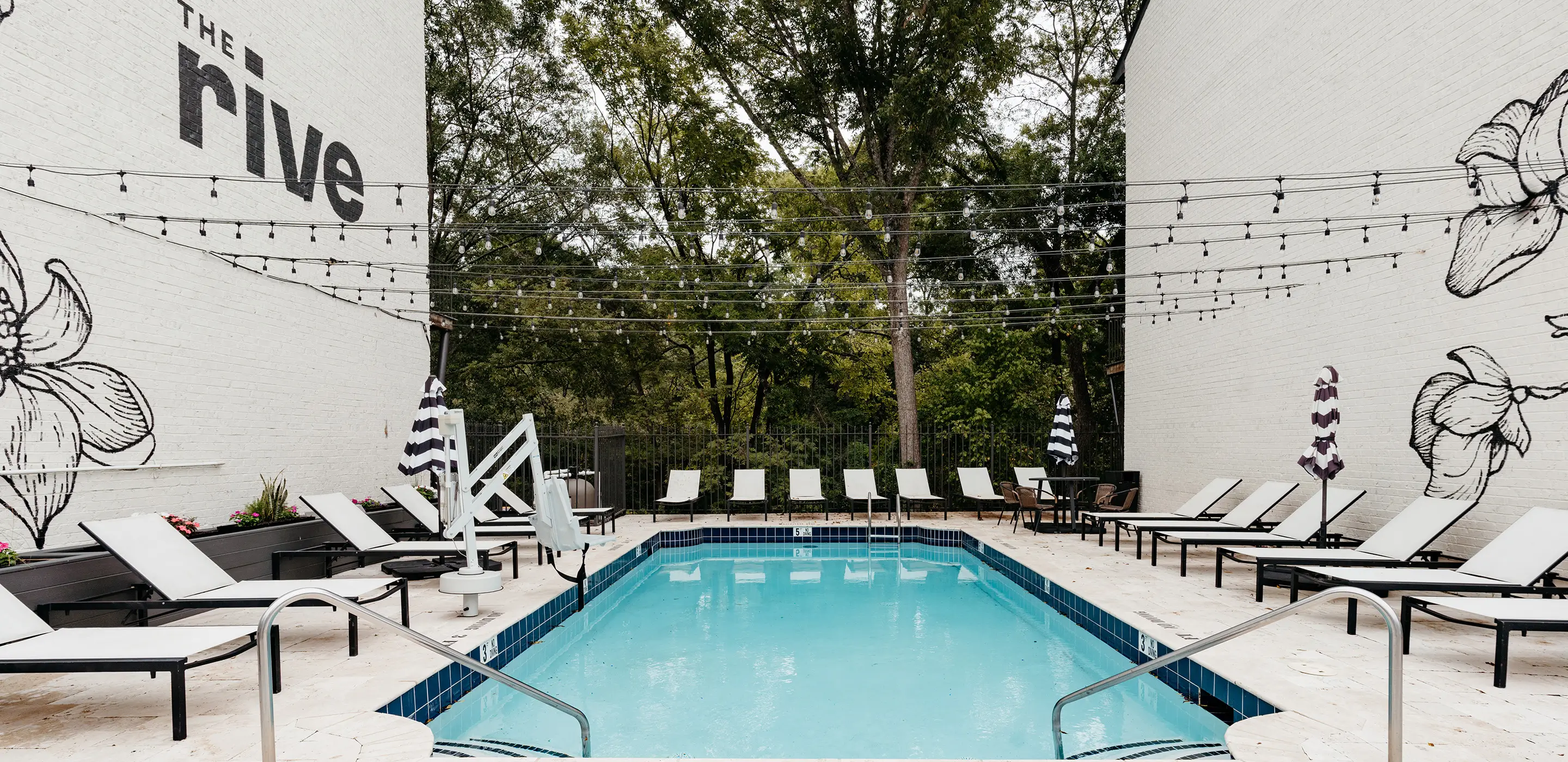 Pool with lounge chairs and umbrellas in front of a white brick mural wall