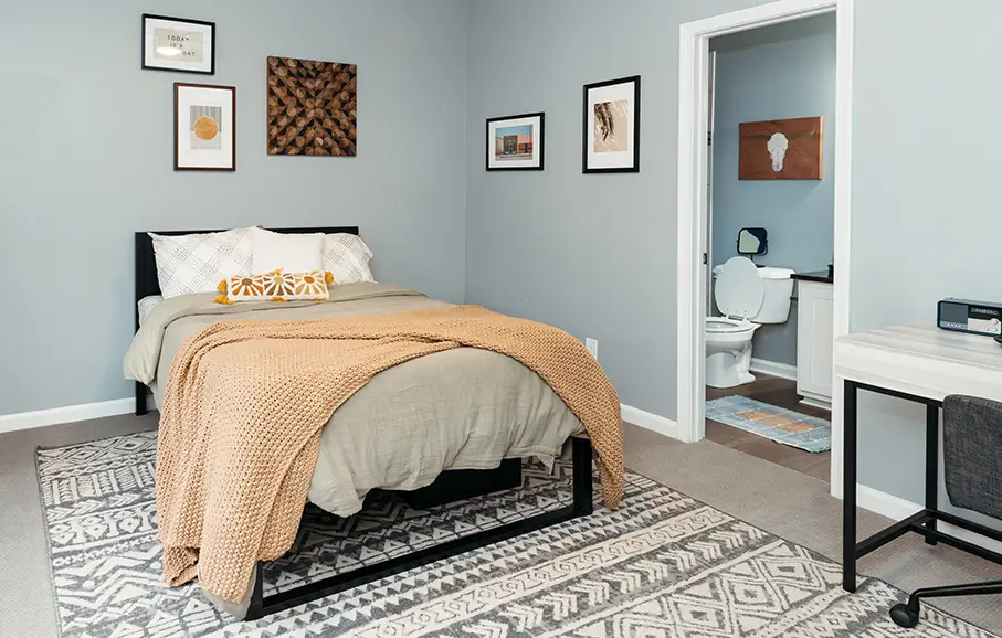 Furnished bedroom with a tan comforter, patterned rug, and framed art