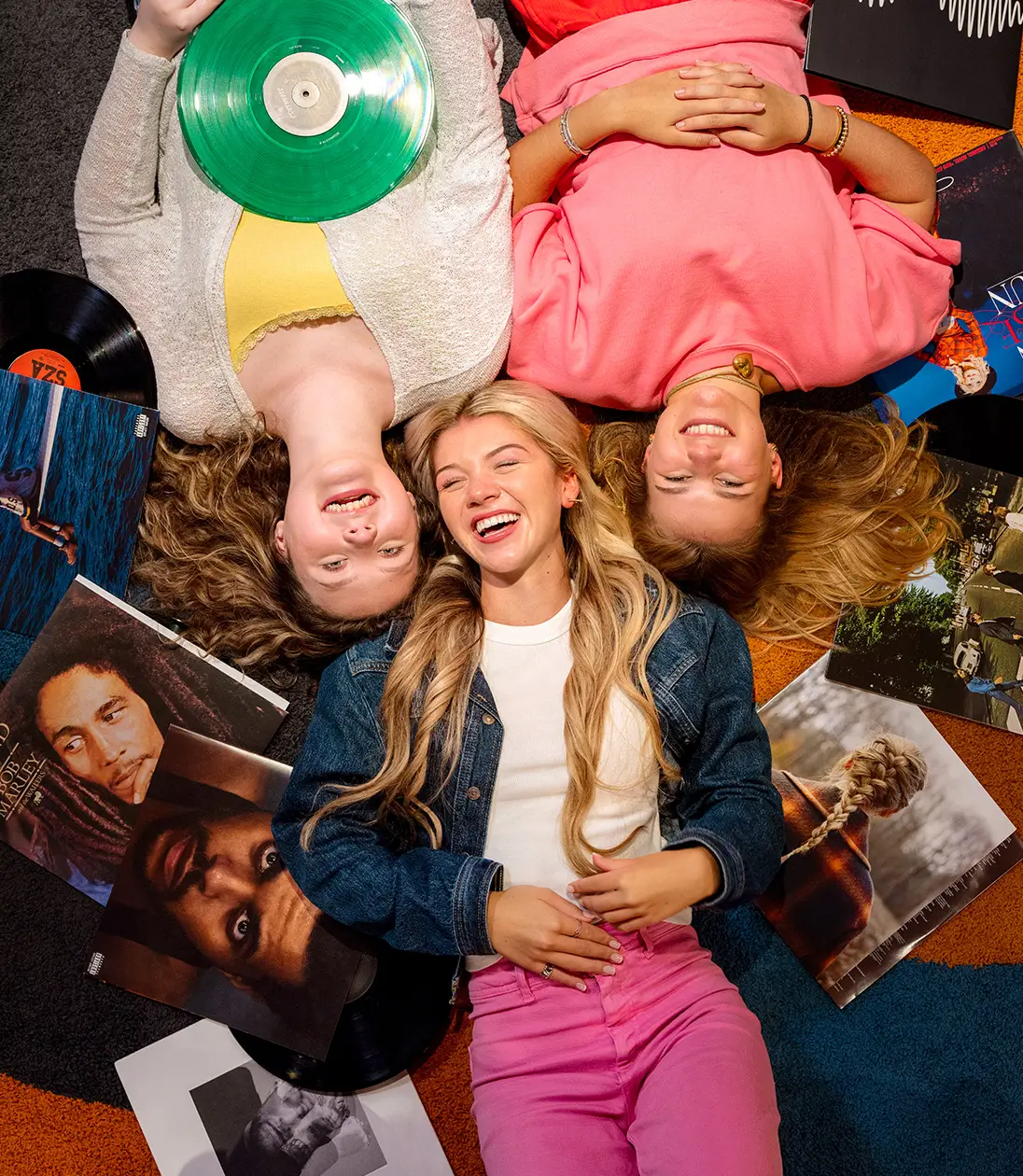A group of young adults smile and laugh while lying on the floor and posing for a photo from above